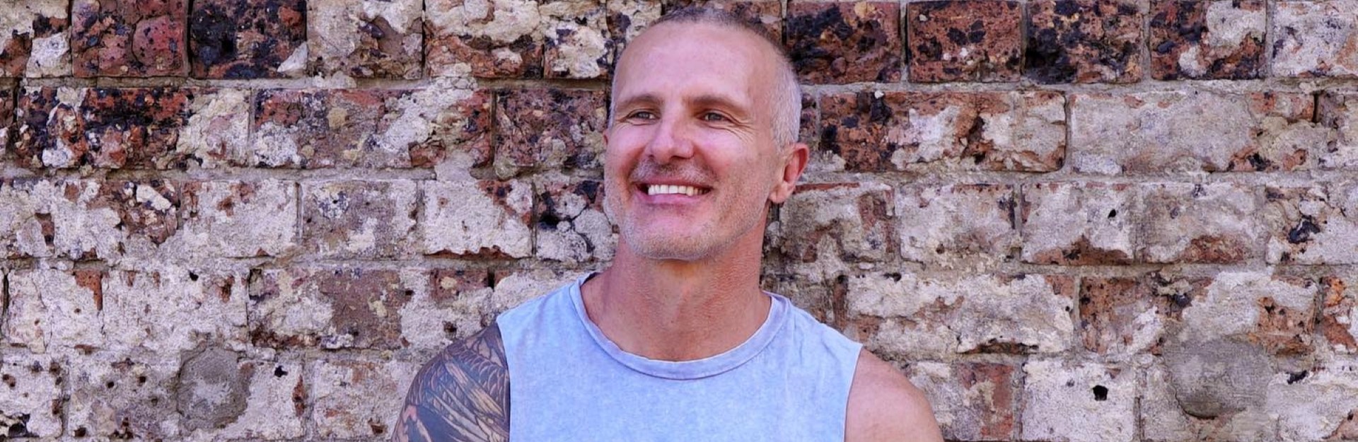 An attractive man sitting in front of a brick wall in a cross-legged yoga pose