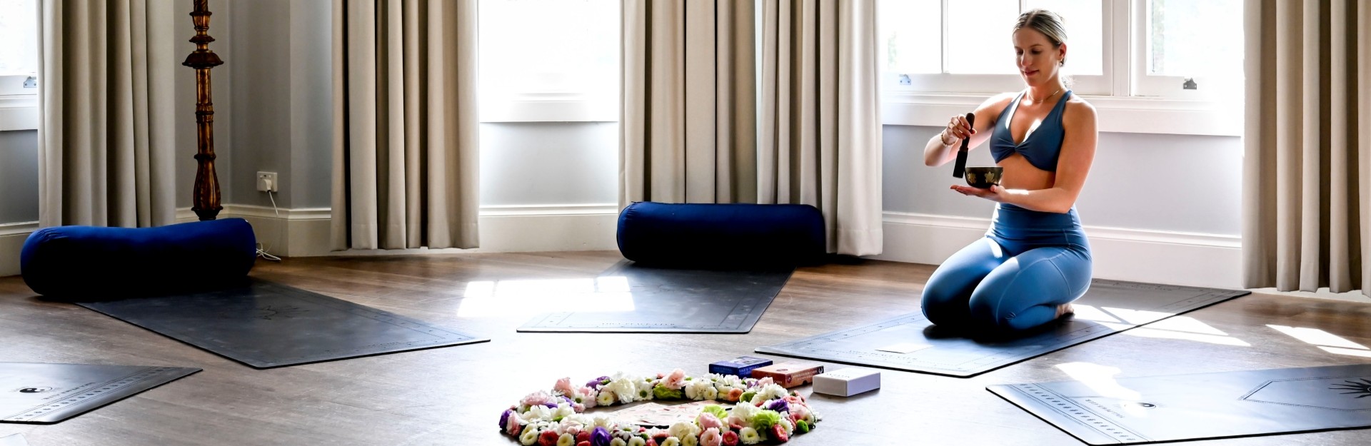 a yoga teacher sitting in a room with yoga mats and a playing a singing bowl