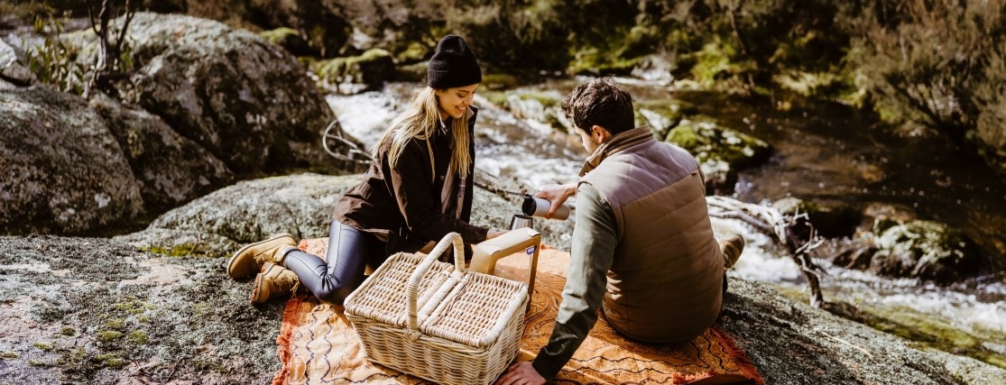 a young couple sitting near a stream with a picnic blanket