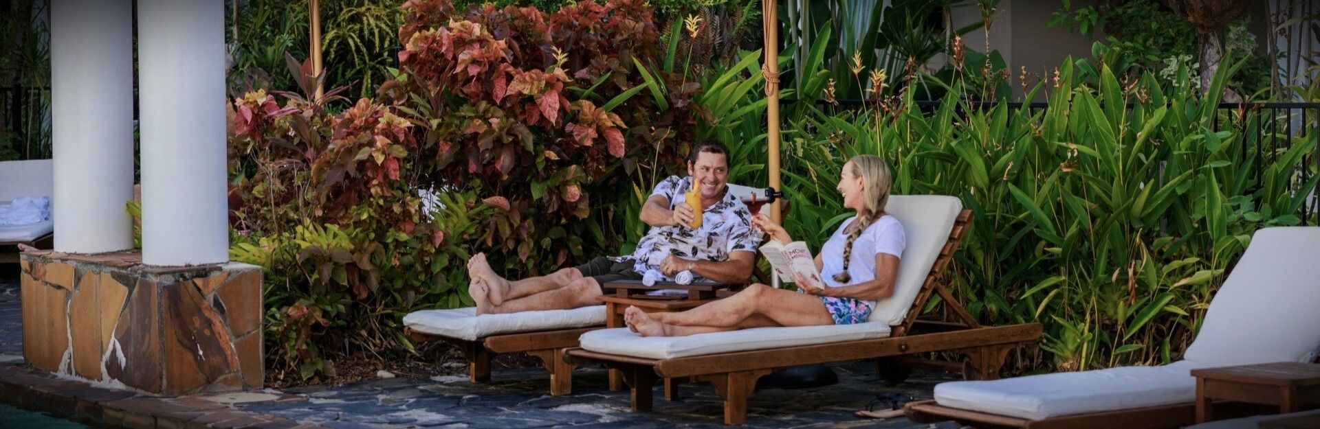 a couple relaxing on sun lounges near a pool with a cocktail