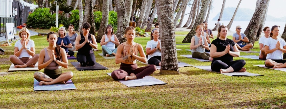 A group of women meditating under palm trees near the beach