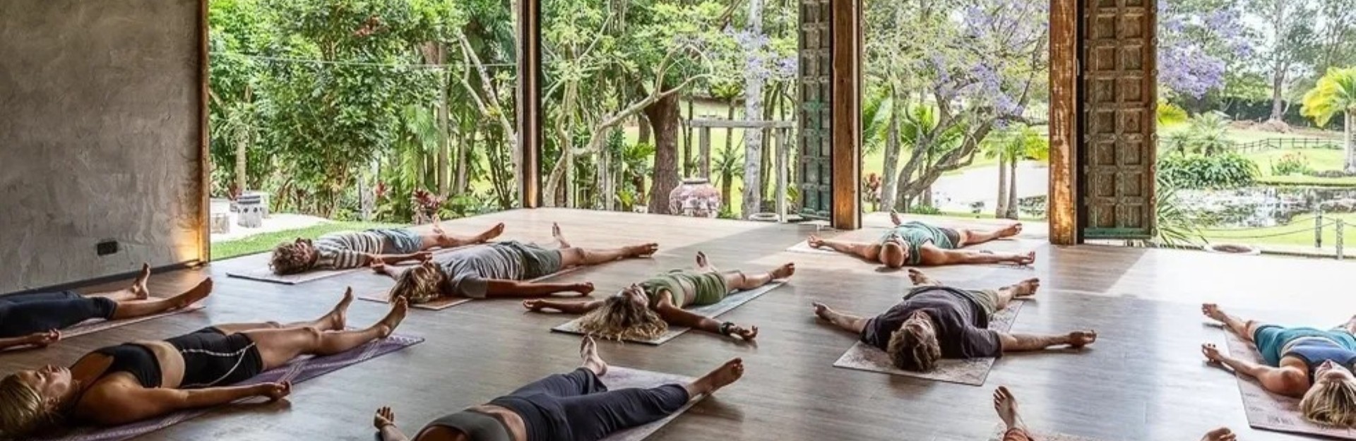 A group of people lying on their backs on yoga mats in an open air yoga room, surrounded by tropical plants