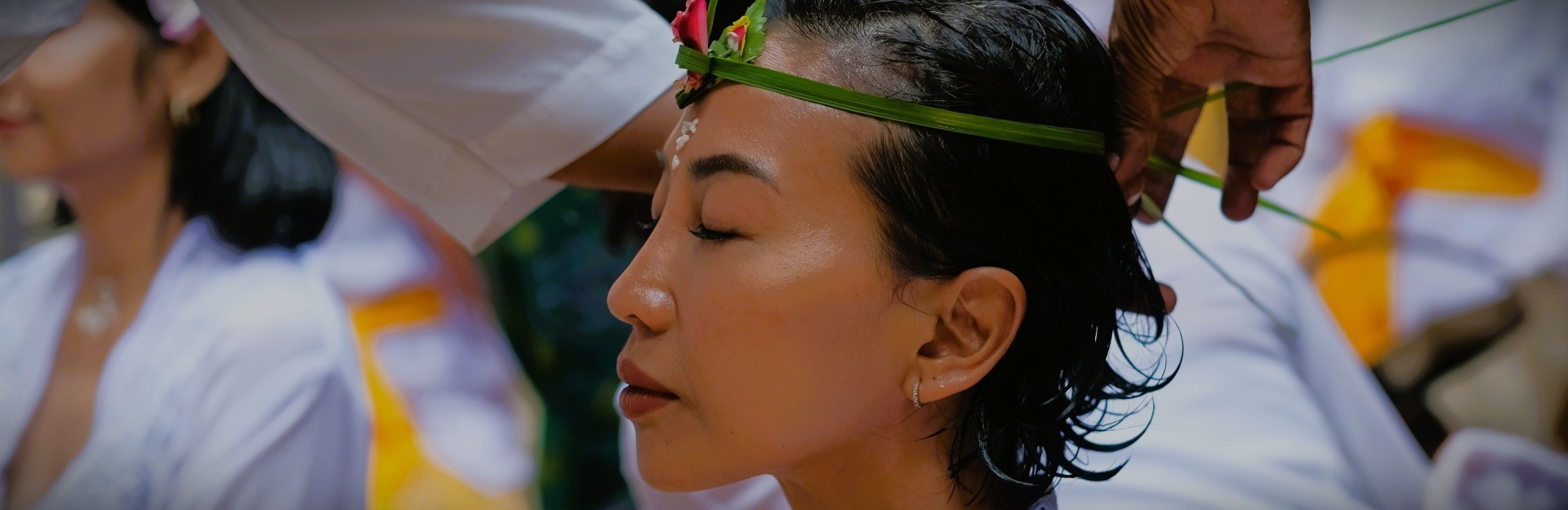 a Balinese woman with her eyes closed, having a handmade headband placed around her head