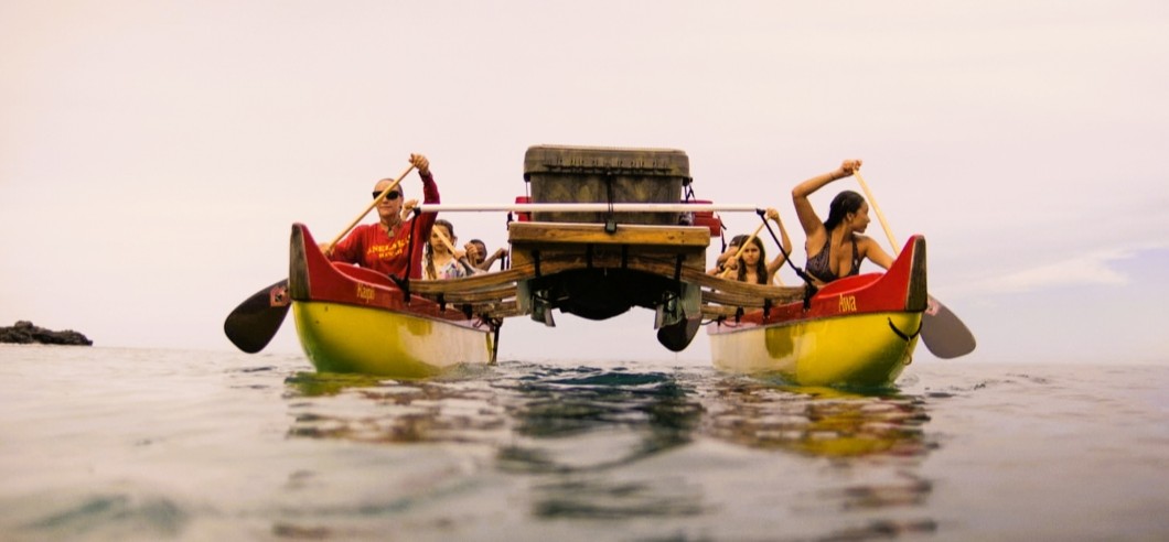 A group of people paddling in a traditional Hawaiian double hull canoe