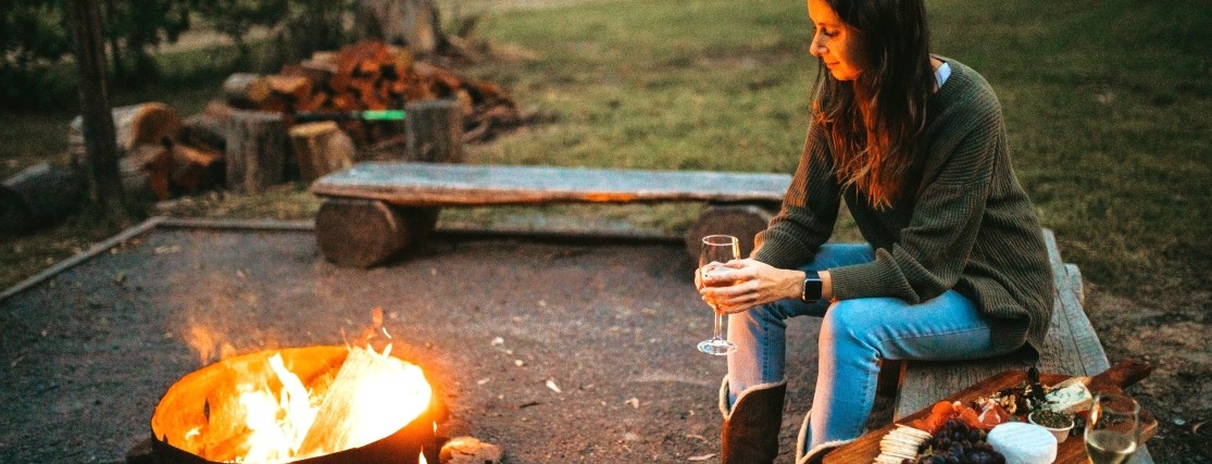 a woman sitting next to a fire pit with a glass of wine