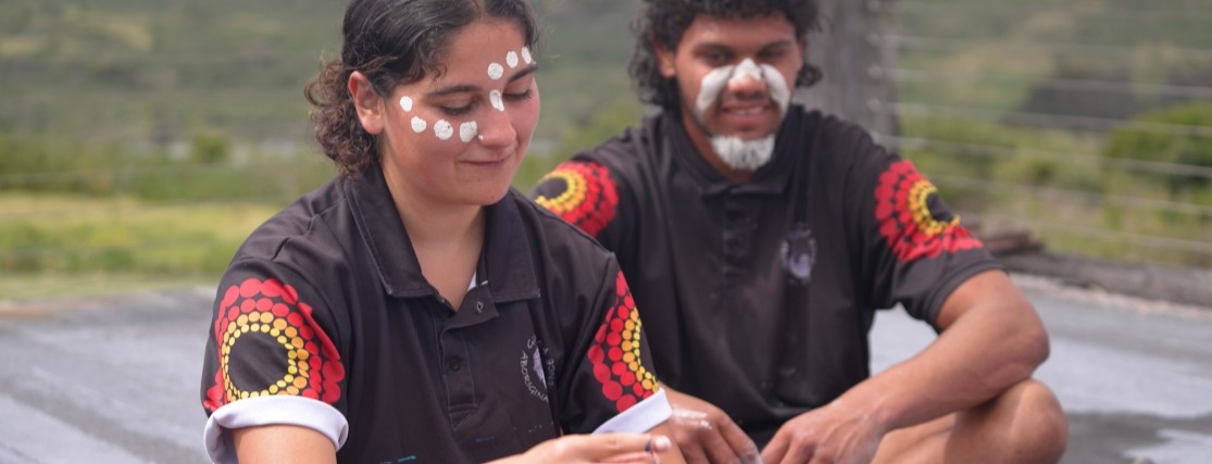 two aboriginal people weaving a bracelet
