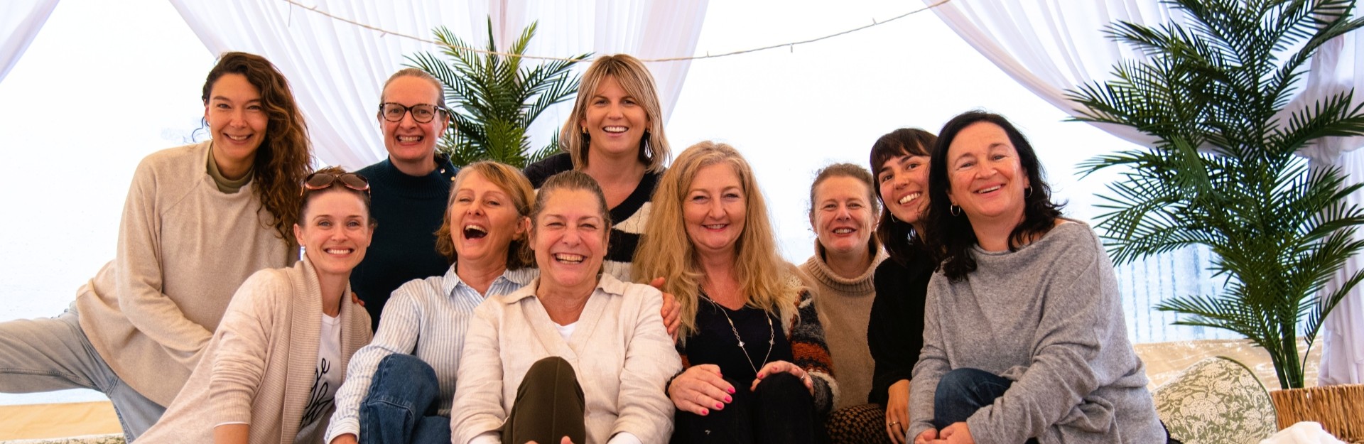a group of smiling women sitting in a large tent during a wellness retreat