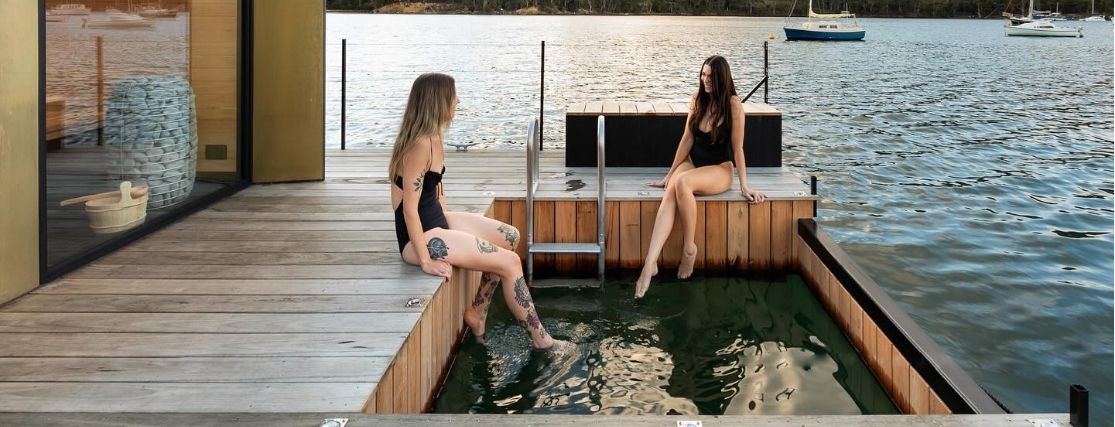 2 ladies sitting on the edge of a deck of a floating sauna