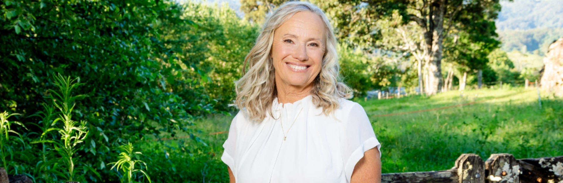 Nutritionist Cindy O'Meara wearing white and standing in front of a wooden gate in a green field