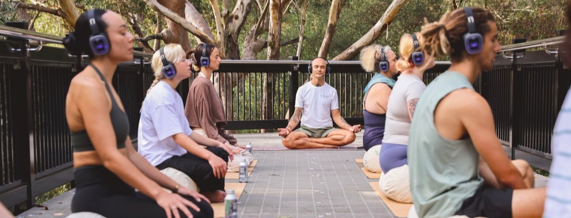 a group of people sitting cross-legged, eyes closed and listeining to headphones