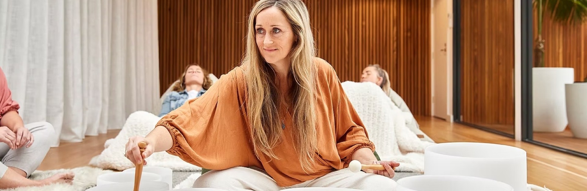 a blonde lady playing crystal singing bowls on the floor in a circle of people