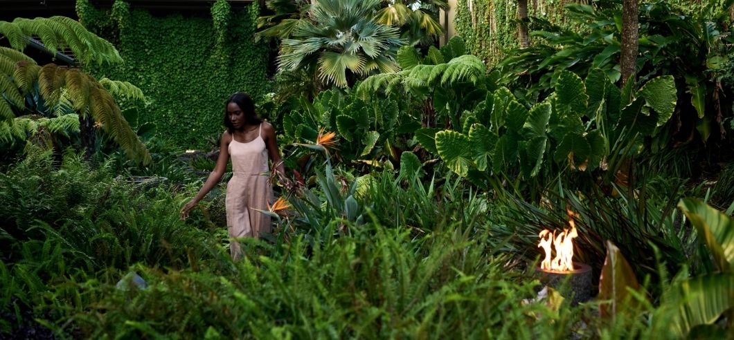 a lady in a pink dress walking through a lush garden