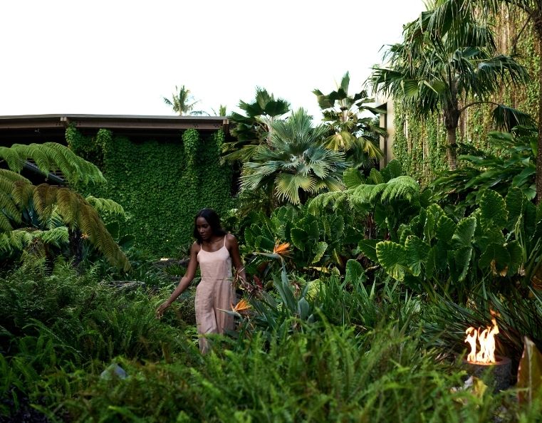 a lady in a pink dress walking through a lush garden