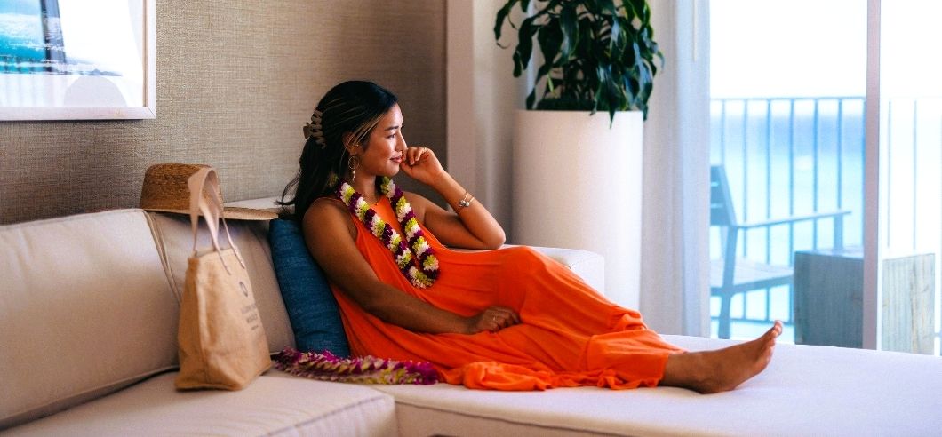 A lady in an orange dress sitting in a hotel room overlooking the pacific ocean