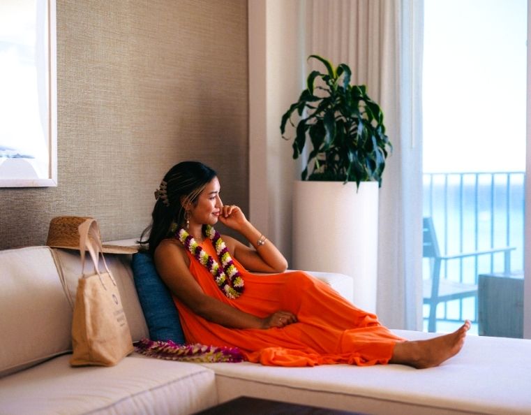 A lady in an orange dress sitting in a hotel room overlooking the pacific ocean