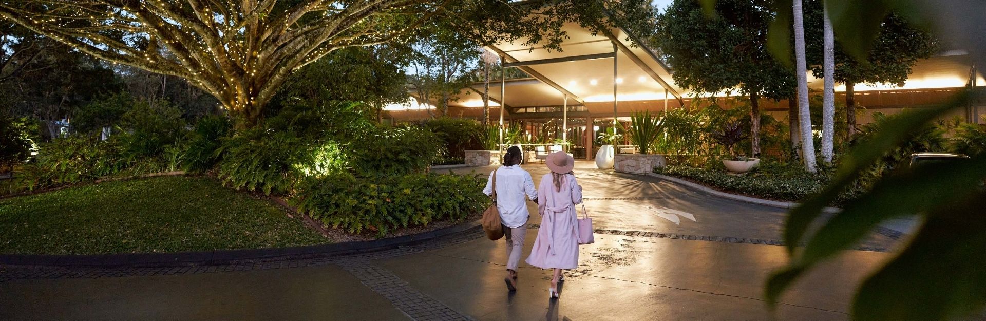 a couple walking towards a tropical resort lobby in the early evening