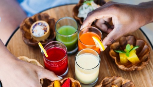 an aerial view of a plate of healthy snacks and drinks, with 2 hands reaching for an item