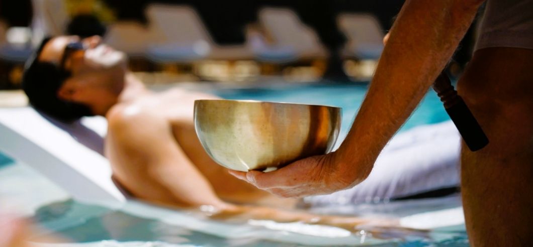a lady lying on a lounge under an umnbrella near an infinity pool, she's enjoying a shoulder massage