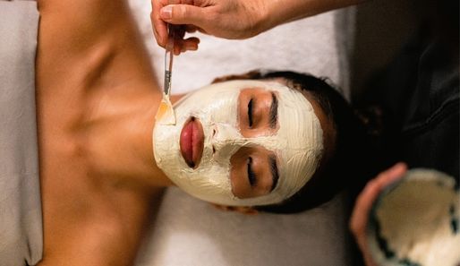 a lady lying on a bed while a therapist applies a face mask in a day spa