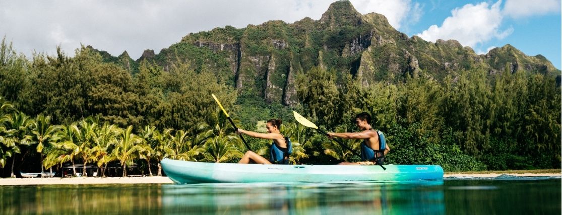 a couple kayaking in hawaii beside a dramatic mountain coastline
