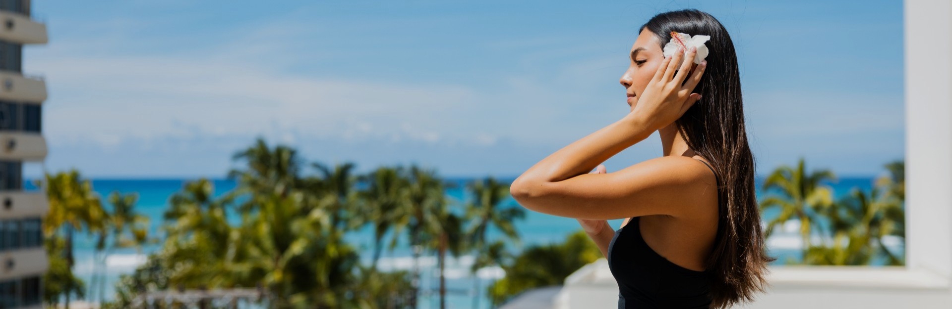 A lady in a black swimsuit putting a flower behind her right ear