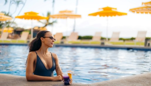 a lady in a black swimsuit relaxing at the edge of a swimming pool with a drink