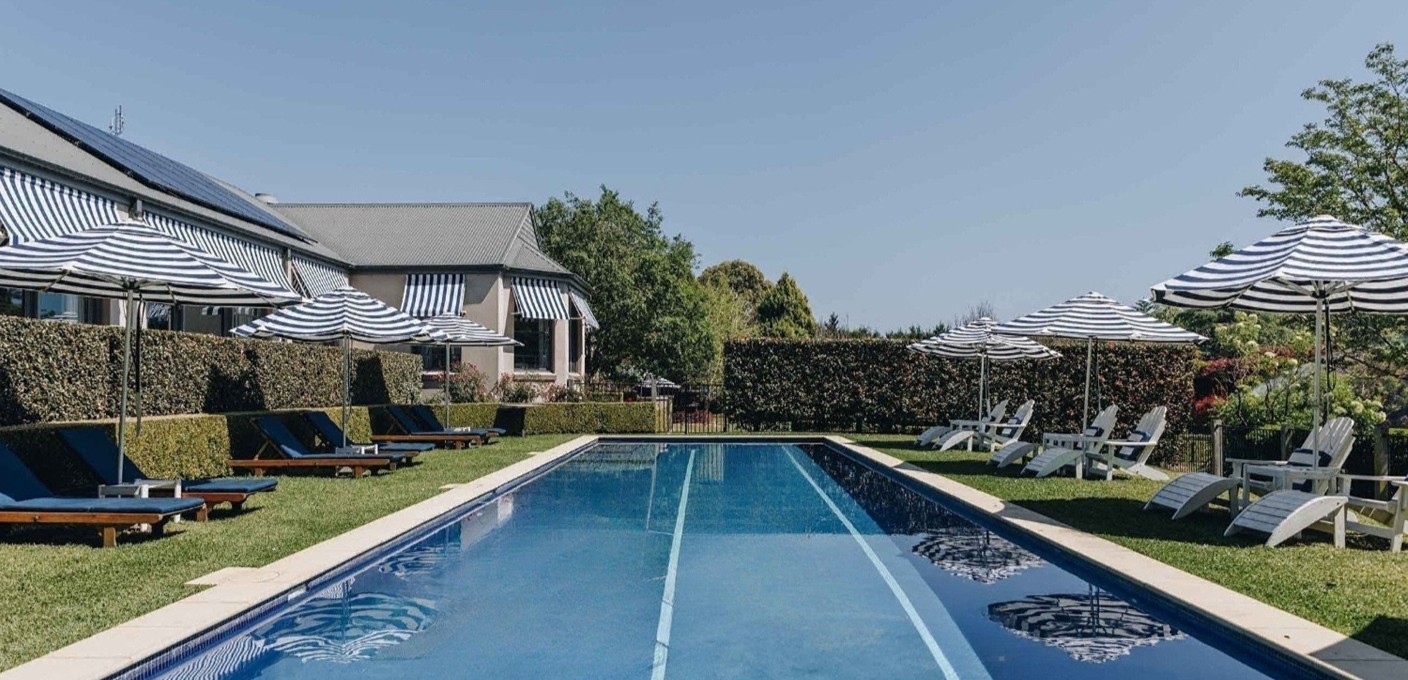 a blue swimming pool surrounded by white deck chairs and blue and white striped umbrellas at Bells at Killcare