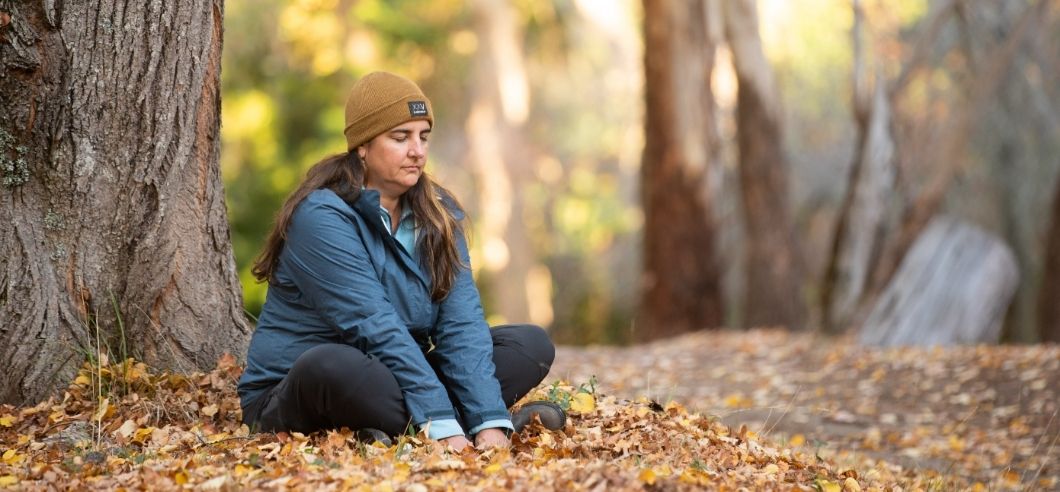 A woman sitting on the ground surrounded by autumn leaves meditating in the Belair State Forest in the Adelaide Hills