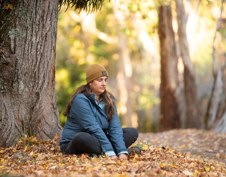 A woman sitting on the ground surrounded by autumn leaves meditating in the Belair State Forest in the Adelaide Hills
