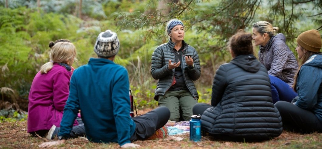 A woman sitting on the ground surrounded by autumn leaves meditating in the Belair State Forest in the Adelaide Hills