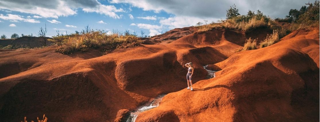 a woman hiking through the red hills of Waimea Canyon in Kauai
