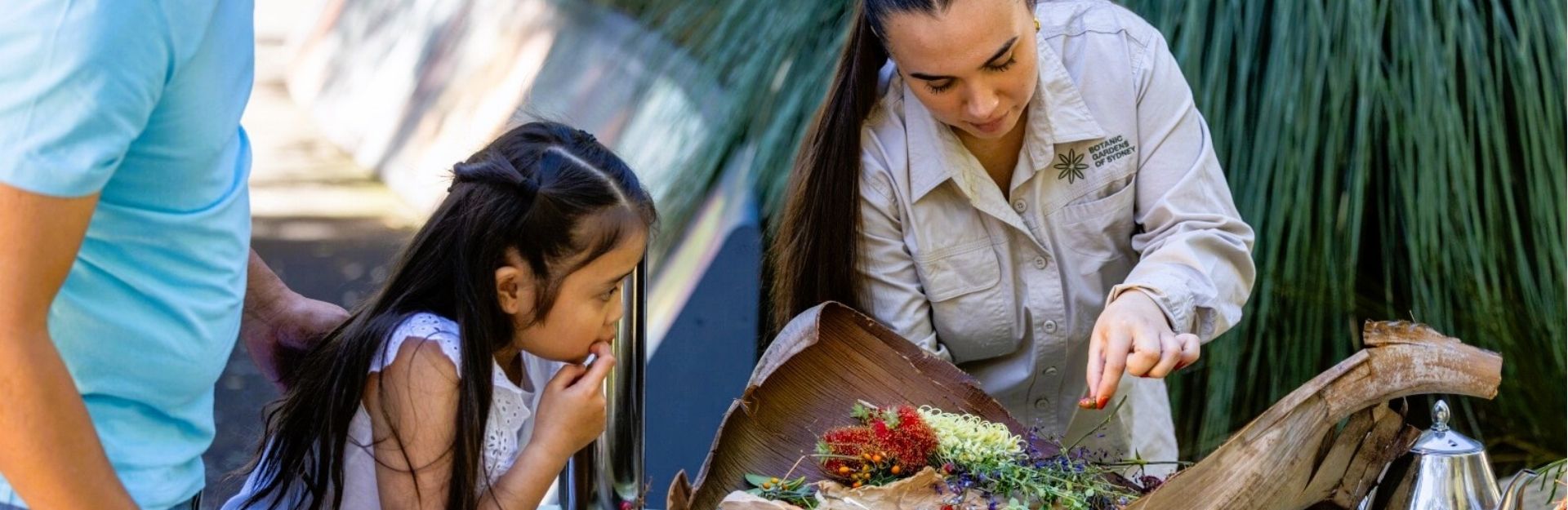 An aboriginal woman showing a young girl a basket of native ingredients at the Royal Botanic Garden Sydney