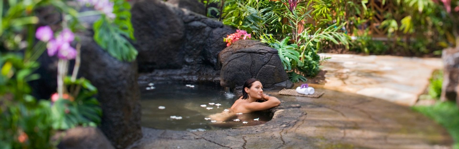 a woman soaking in an outdoor pool at Grand Hyatt Kaua'i surrounded by lush gardens