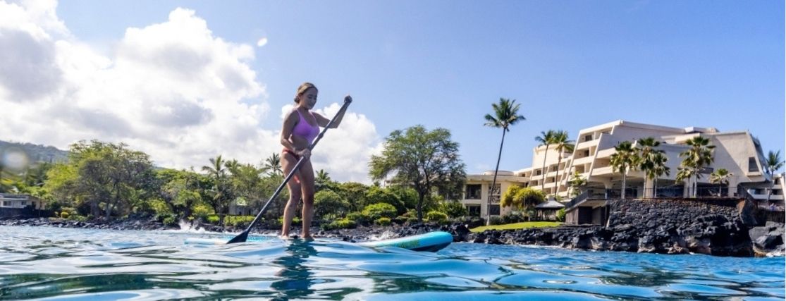 a lady riding a SUP board on the ocean in front of Outrigger Kona Resort & Spa