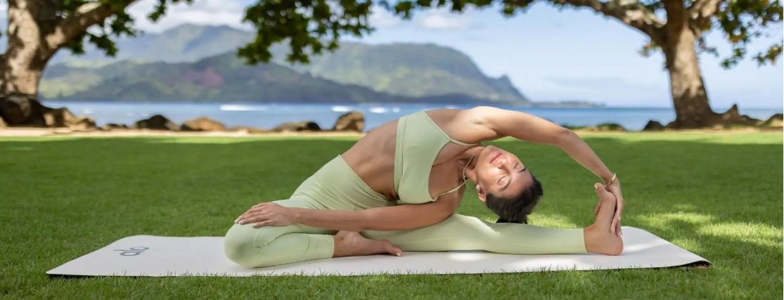 a lady doing yoga outdoors at 1 Hotel Hanalei Bay, with the dramatic coastline behind her