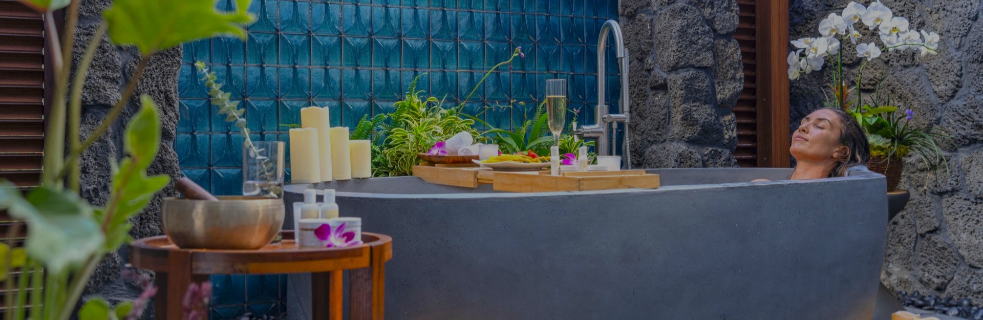 A lady relaxing in an outdoor bath, surrounded by flowers and candles