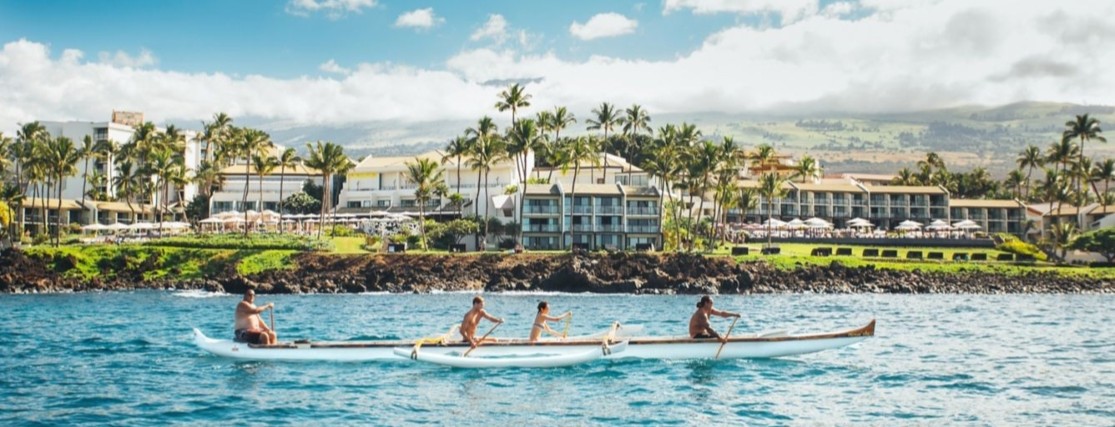a group of people paddling an outrigger canoe in front of a hotel in Maui