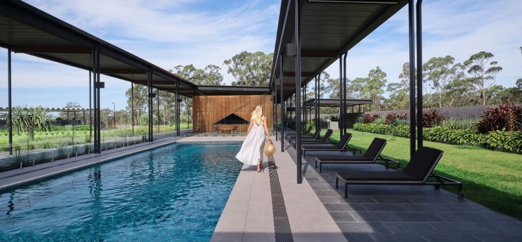 a lady in a flowing white dress walking along the edge of a long blue swimming pool