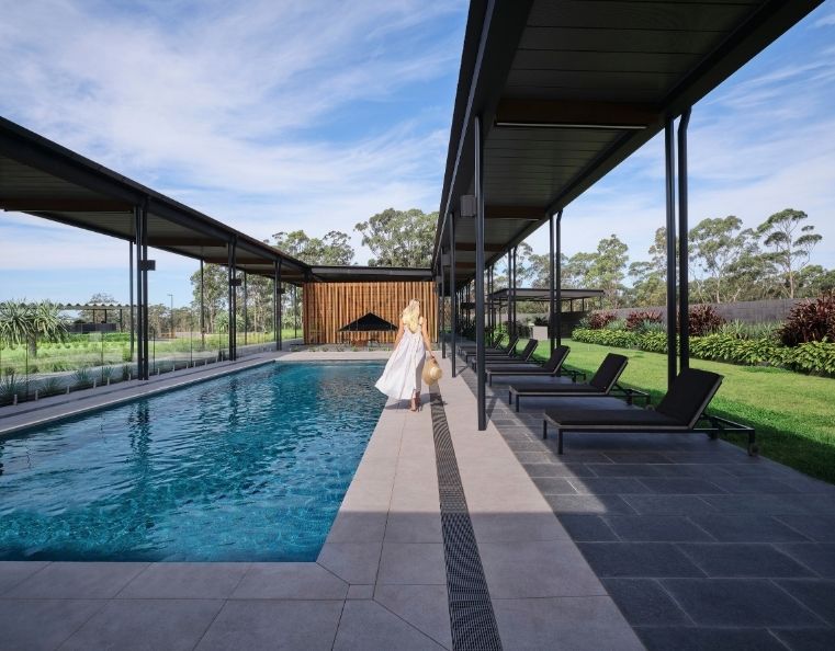 a lady in a flowing white dress walking along the edge of a long blue swimming pool