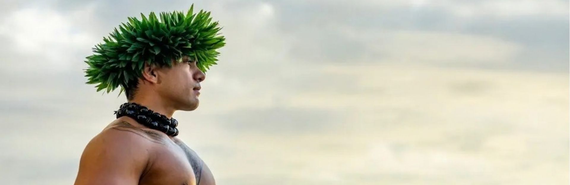 a Hawaiian man wearing a green head dress looking out to see